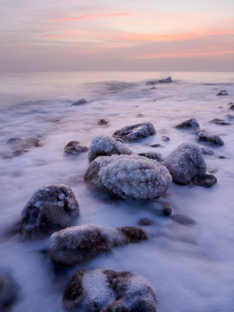 Salt-encrusted rocks along the shoreline of the Dead Sea, softened by wave motion blur at sunrise.