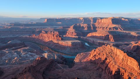 A sweeping aerial view of red sandstone canyons and a horseshoe bend of the Colorado River at sunrise.