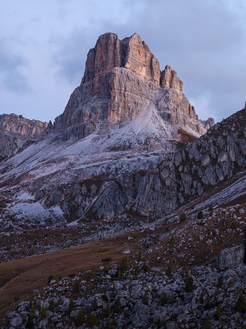 A single sharp limestone peak rising above rocky slopes under a soft evening sky.