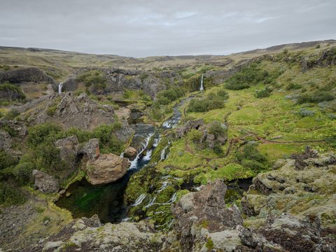 A lush green volcanic valley with small waterfalls cutting through mossy rock formations.