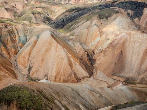 Close aerial view of Landmannalaugar's rhyolite mountains, showing bands of orange, green, and black volcanic rock.